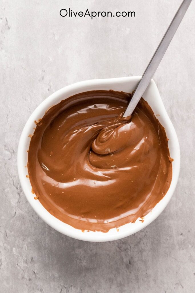 Melted milk chocolate in a white bowl for Christmas pretzel bark.