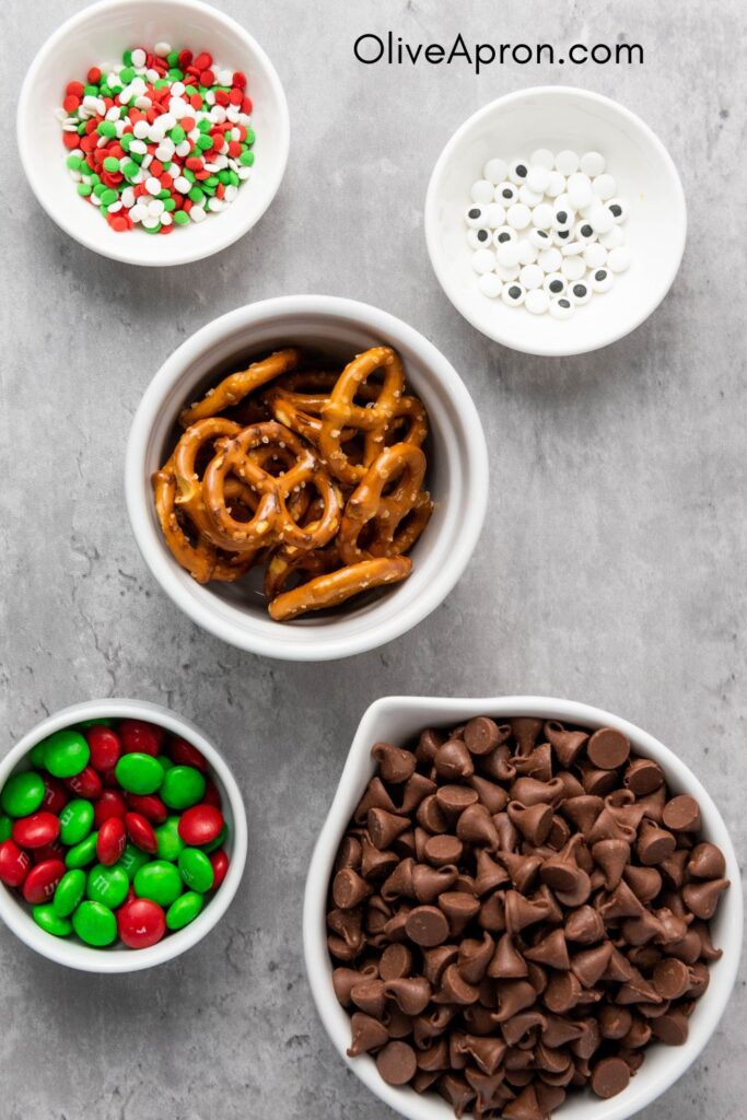 Ingredients for Christmas pretzel bark including chocolate chips, pretzels, candies, and sprinkles.