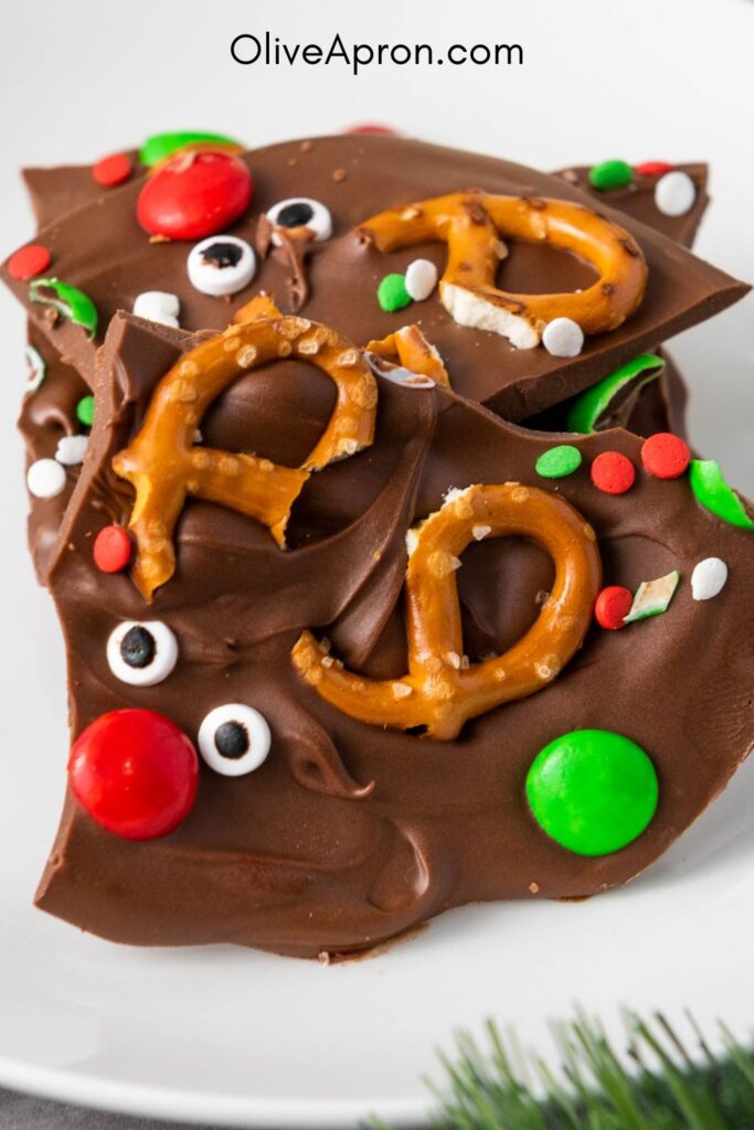 Stacked pieces of Christmas pretzel bark with chocolate, sprinkles, and candy eyes.