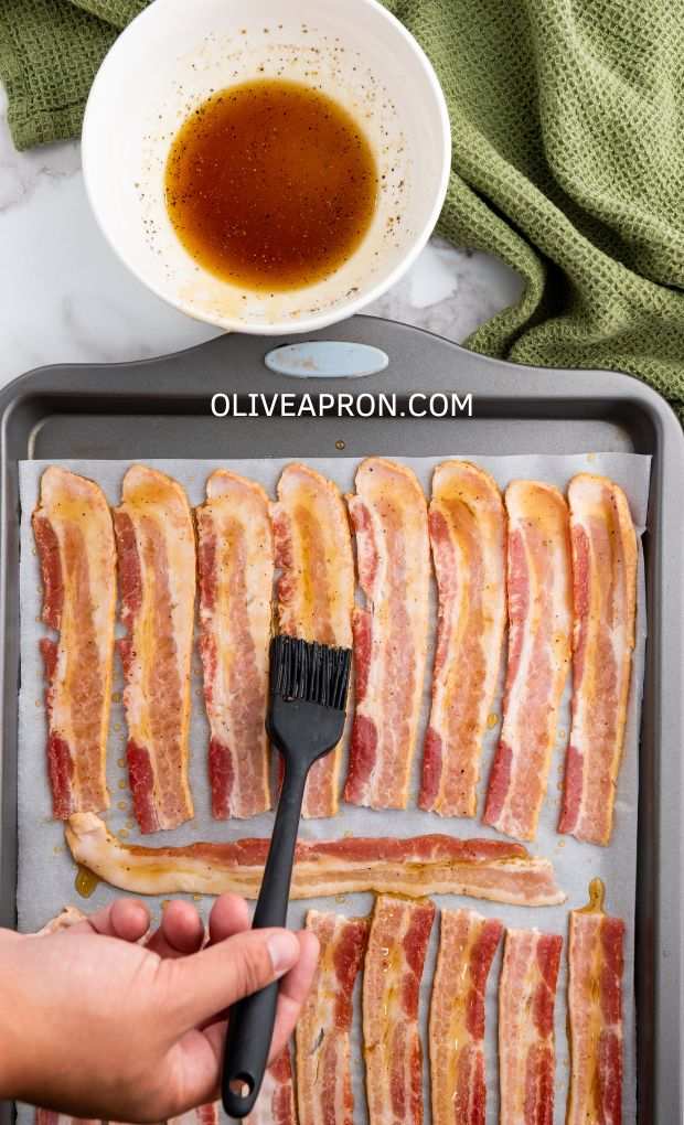 A brush coating bacon slices in a tray.