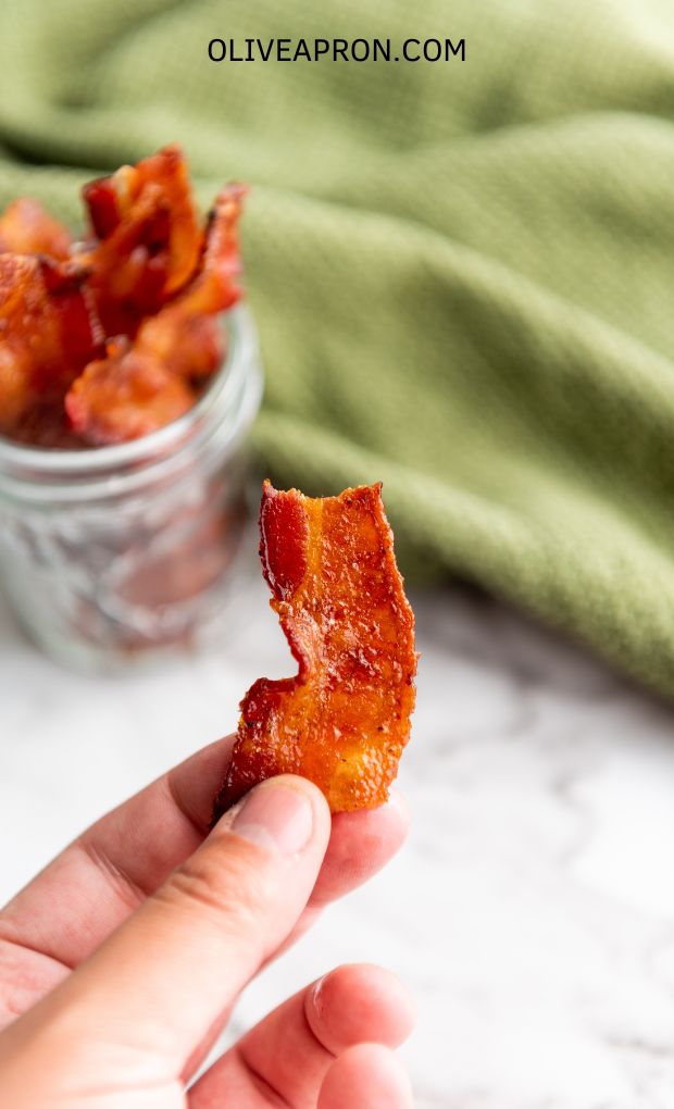 A hand holding a piece of crispy candied bacon.
