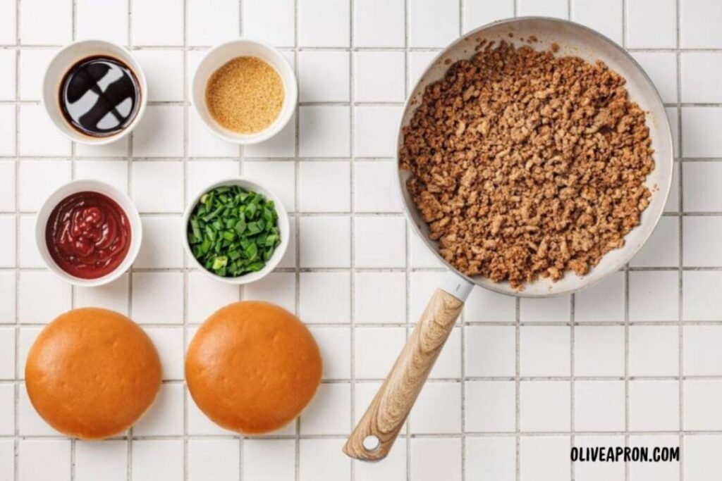 Korean Beef Sloppy Joes Recipe Skillet of seasoned beef with ketchup and sugar added, next to fresh buns and scallions