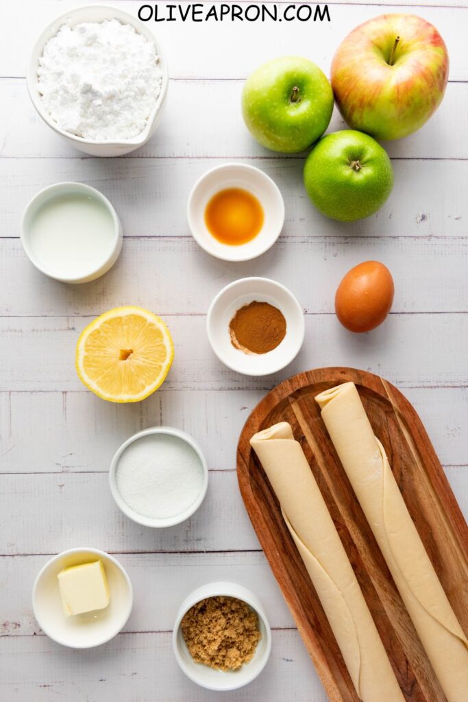Ingredients for homemade apple hand pies with fresh apples, pie crust, cinnamon, lemon, and sugar – easy fall handheld apple dessert.