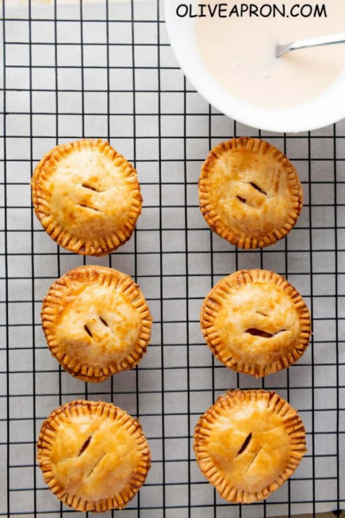 Individual apple pies cooling on a rack – small handheld apple desserts perfect for fall.