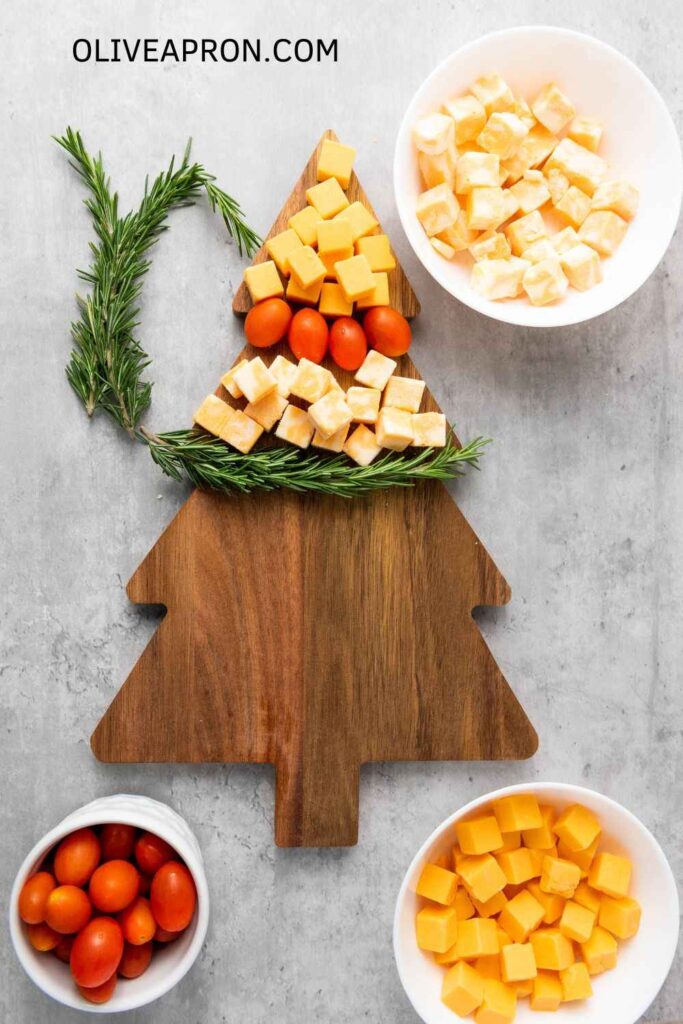 Making a Christmas Tree Cheese with rosemary springs over a Christmas tree board.