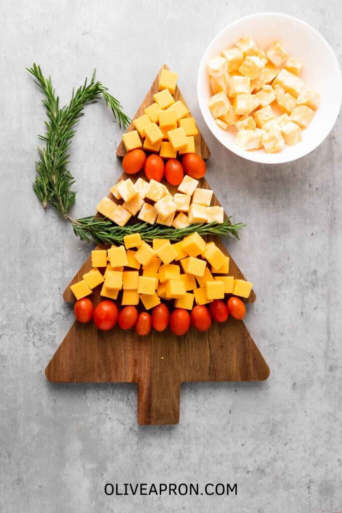 A Christmas Tree Cheese with rosemary springs over a Christmas tree board.