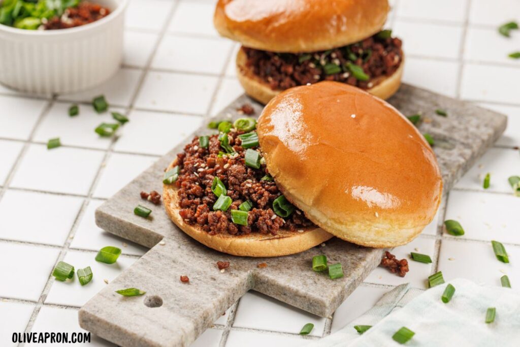 Two sloppy joe sandwiches filled with seasoned ground beef and green onions on a serving board.