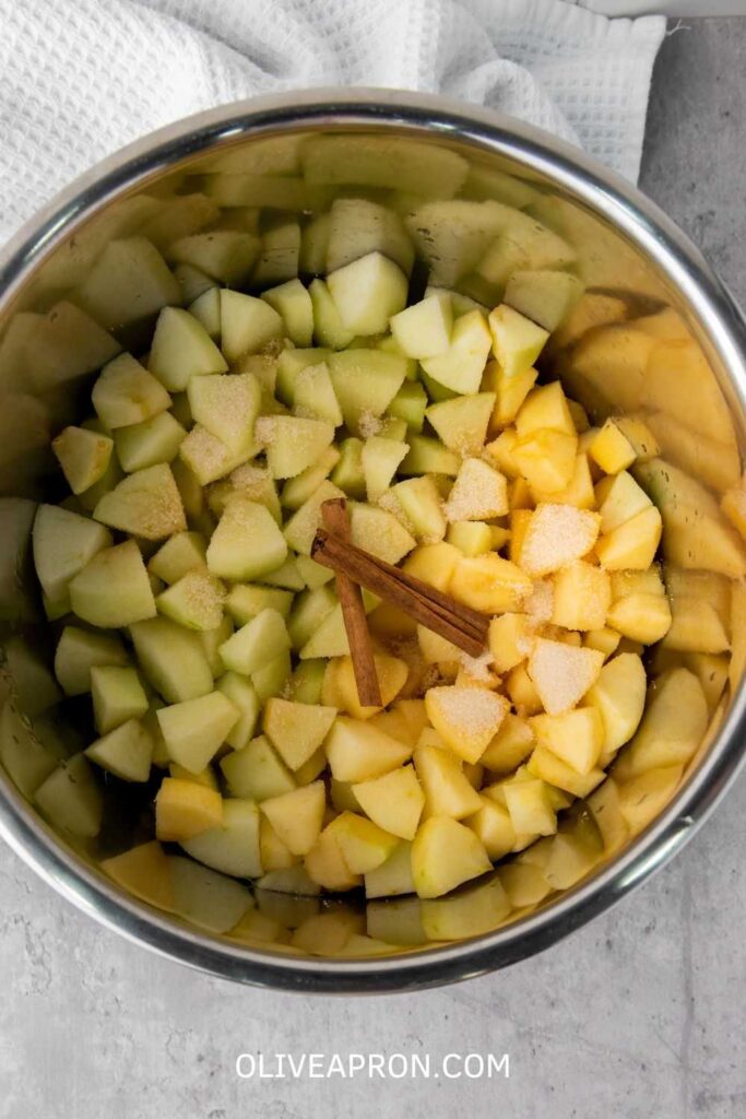 Instant Pot Cinnamon Applesauce Recipe Chopped apples with cinnamon sticks and sugar in an Instant Pot before cooking.