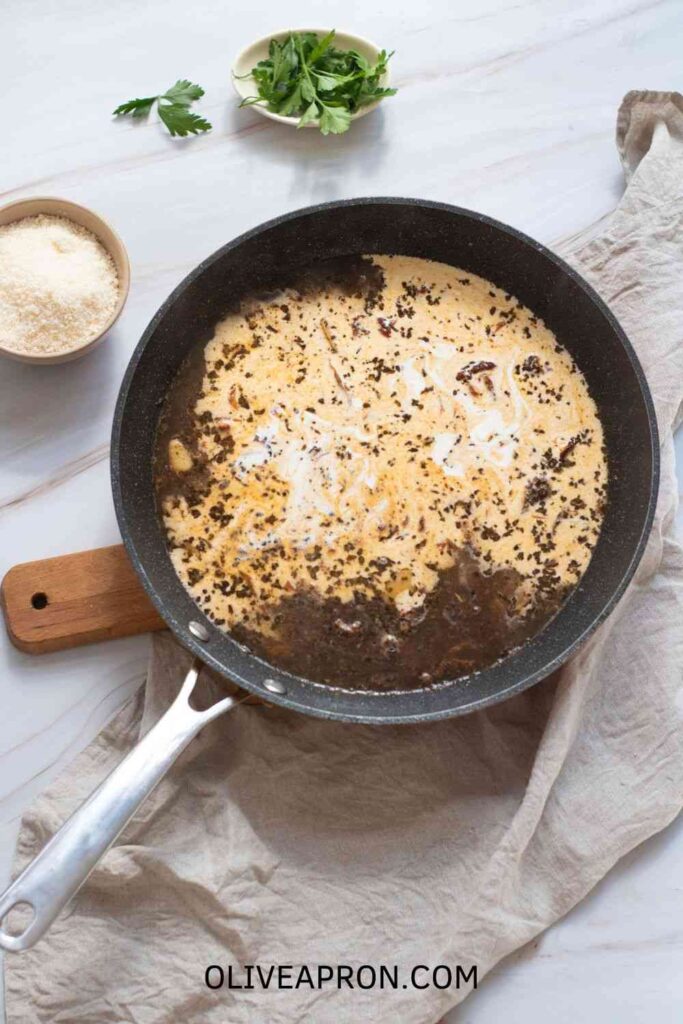 Skillet with creamy Marry Me Chicken sauce simmering with sun-dried tomatoes, herbs, and cream, surrounded by Parmesan and fresh parsley.