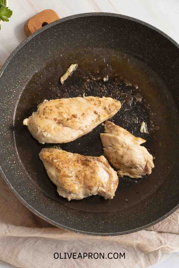 Golden seared chicken breasts cooking in a skillet before adding the creamy Marry Me Chicken sauce.