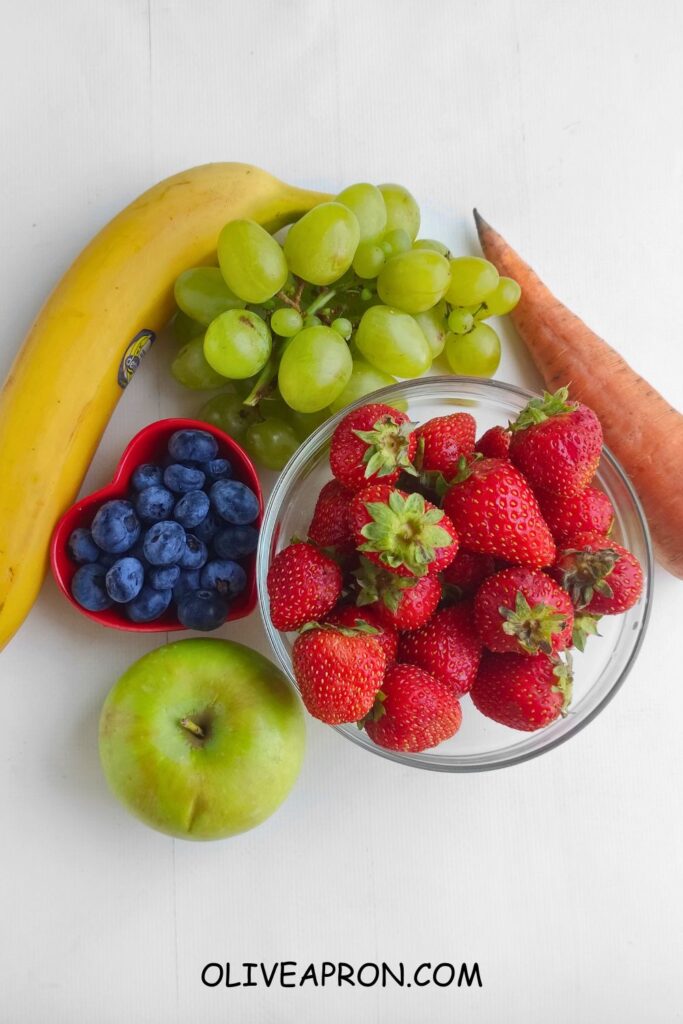 Banana, apple, grapes, blueberries, strawberries, and carrot on a white background.
