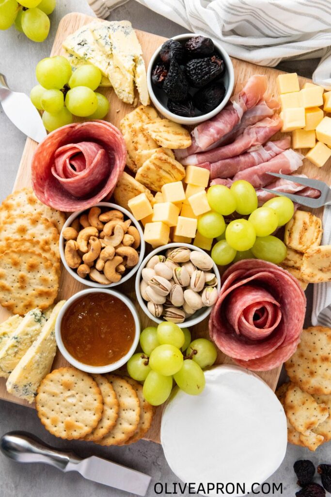 Close-up of a festive charcuterie board with grapes, blue cheese, salami roses, and mixed nuts.