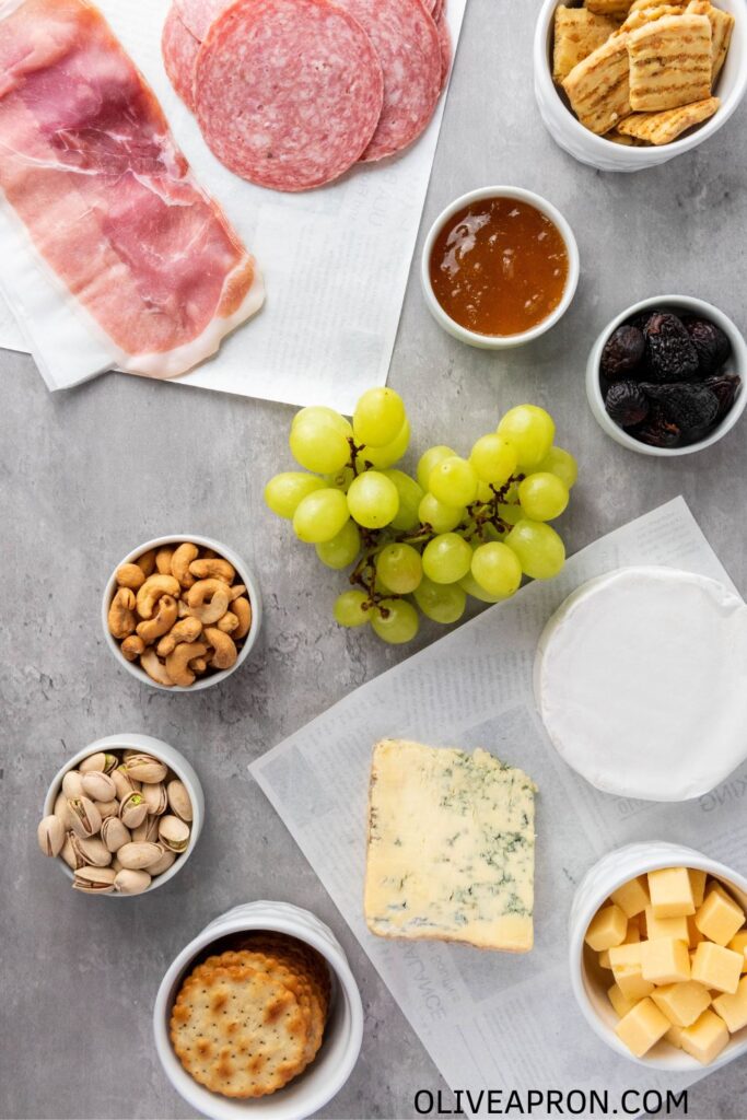 Charcuterie board ingredients including cheeses, cured meats, grapes, crackers, nuts, and fig jam.