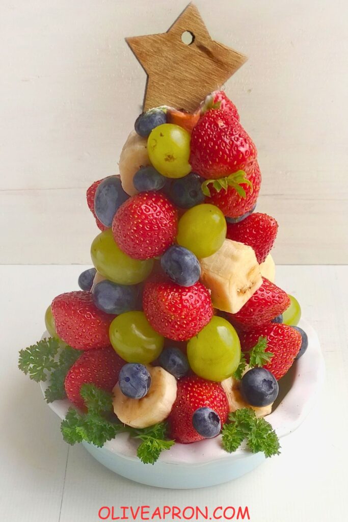 Close-up of a fruit Christmas tree topped with a wooden star and dusted with powdered sugar.
