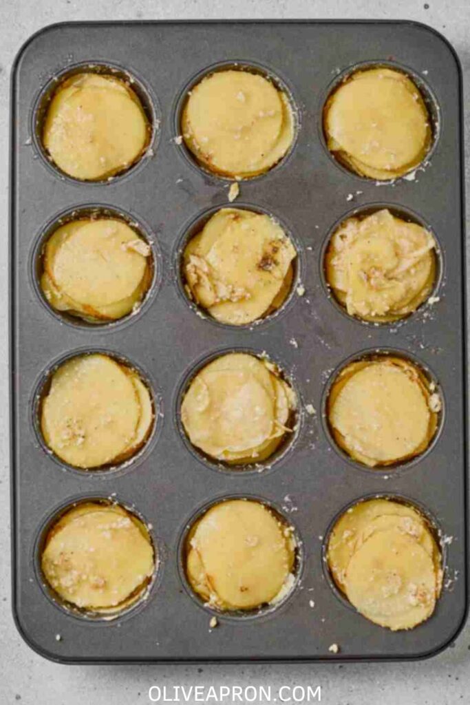 Thin potato layers stacked in muffin tin before baking parmesan garlic potato stacks.