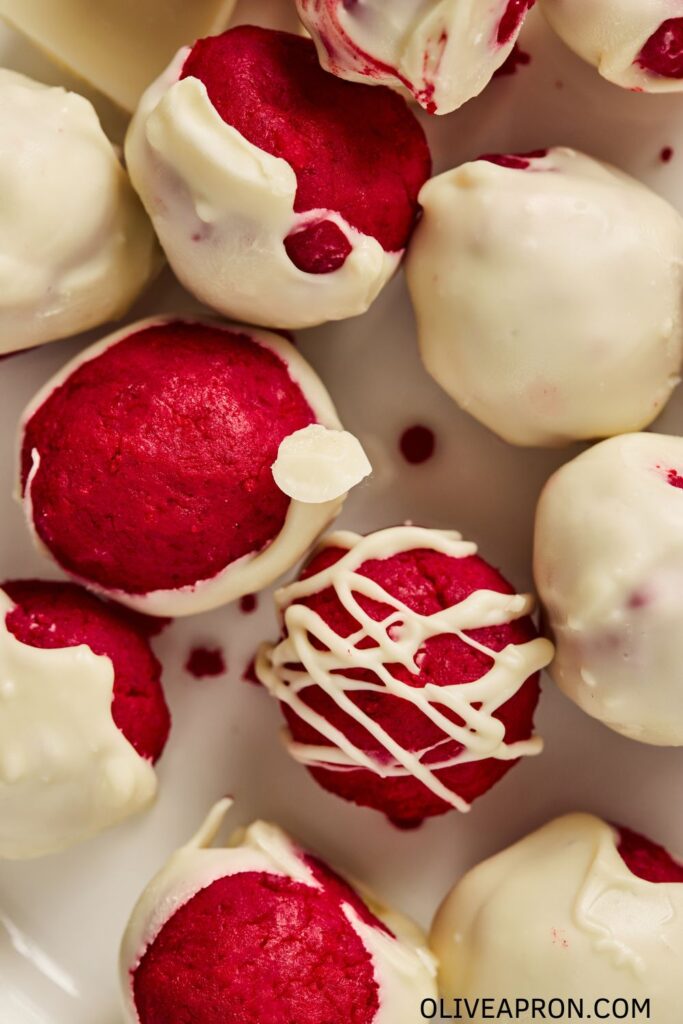 Close up of red velvet truffles coated in white chocolate with a creamy red center.