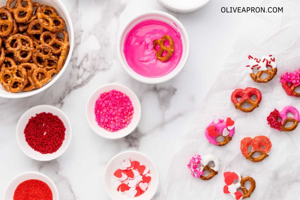 Valentine pretzels in a bowl and candy melts and sprinkles in bowls.