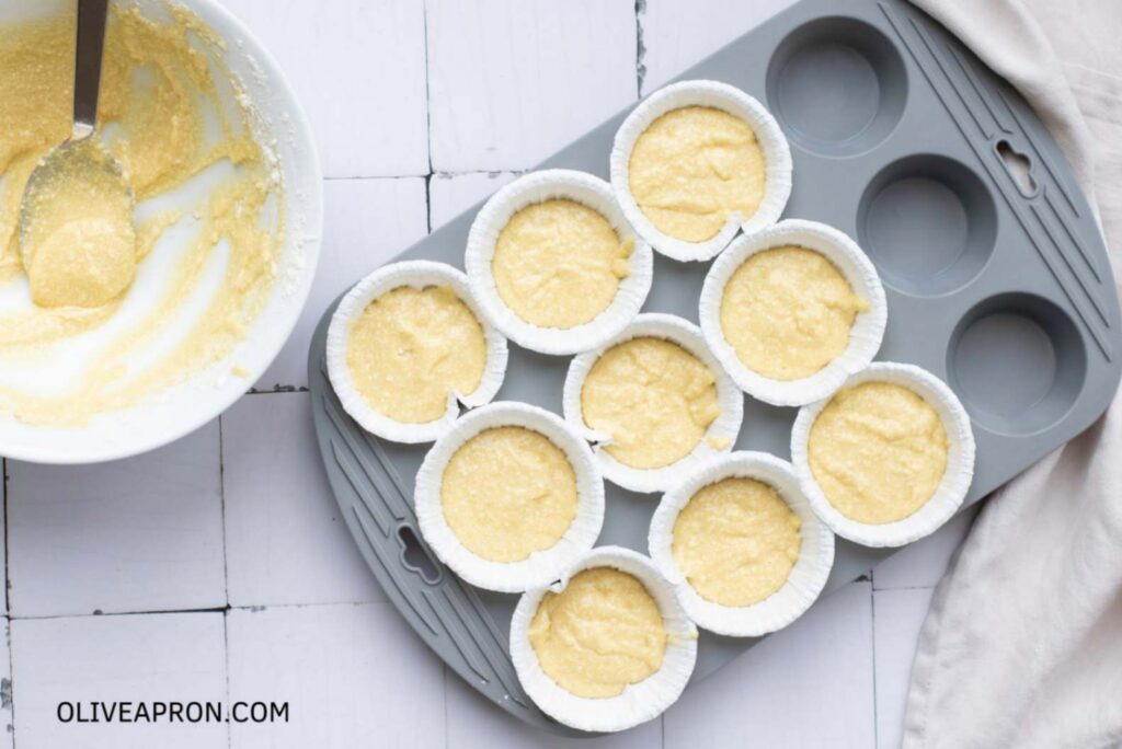 Vanilla cupcake batter portioned into paper liners inside a muffin tin, ready to bake.