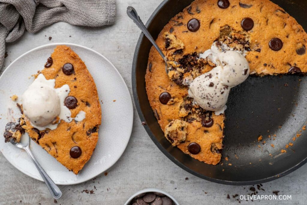 Cookie skillet ice cream with a spoon and a slice of chocolate chip cookie slice on a plate with ice cream.