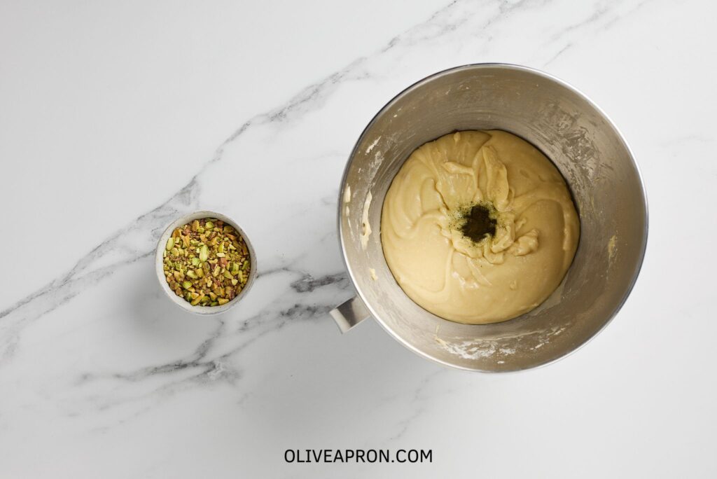 Green food coloring in cupcake mixture and a small bowl with pistachios